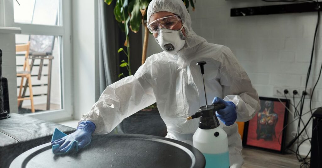 A person in full PPE disinfects an indoor surface to prevent COVID-19.